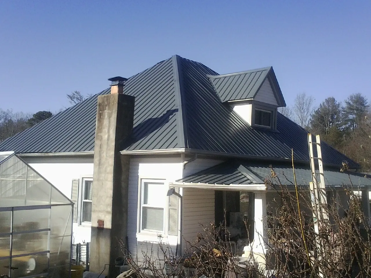 Dark blue standing seam metal roof on a white farmhouse with dormer — Slate & Tile Roof Repair by Roofing Brothers in Tunica