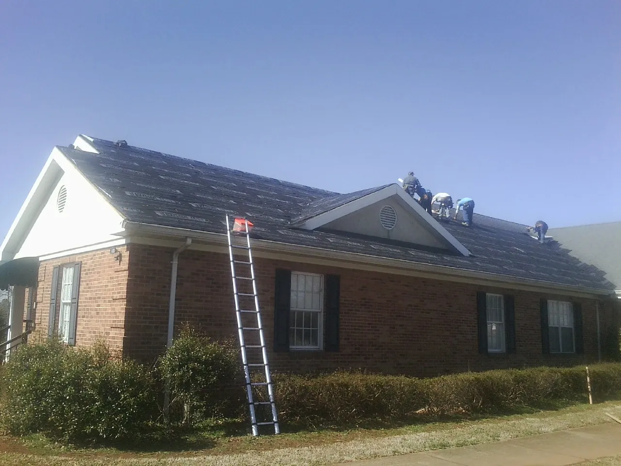 Crew tearing shingles off a brick ranch roof with a ladder set — Emergency Roof Repair work by our crew in Tunica