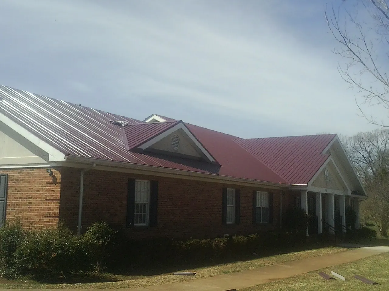 Red metal roof with gabled entries on a long brick building, from a Hail Damage Roof Repair job in Tunica