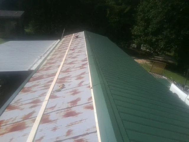 Old rusted panels beside newly installed green metal roofing — Wind Damage Roof Repair by Roofing Brothers in Tunica