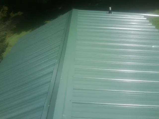 New green metal panels meeting at the ridge of a roof — Flat Roof Repair work by our crew in Tunica