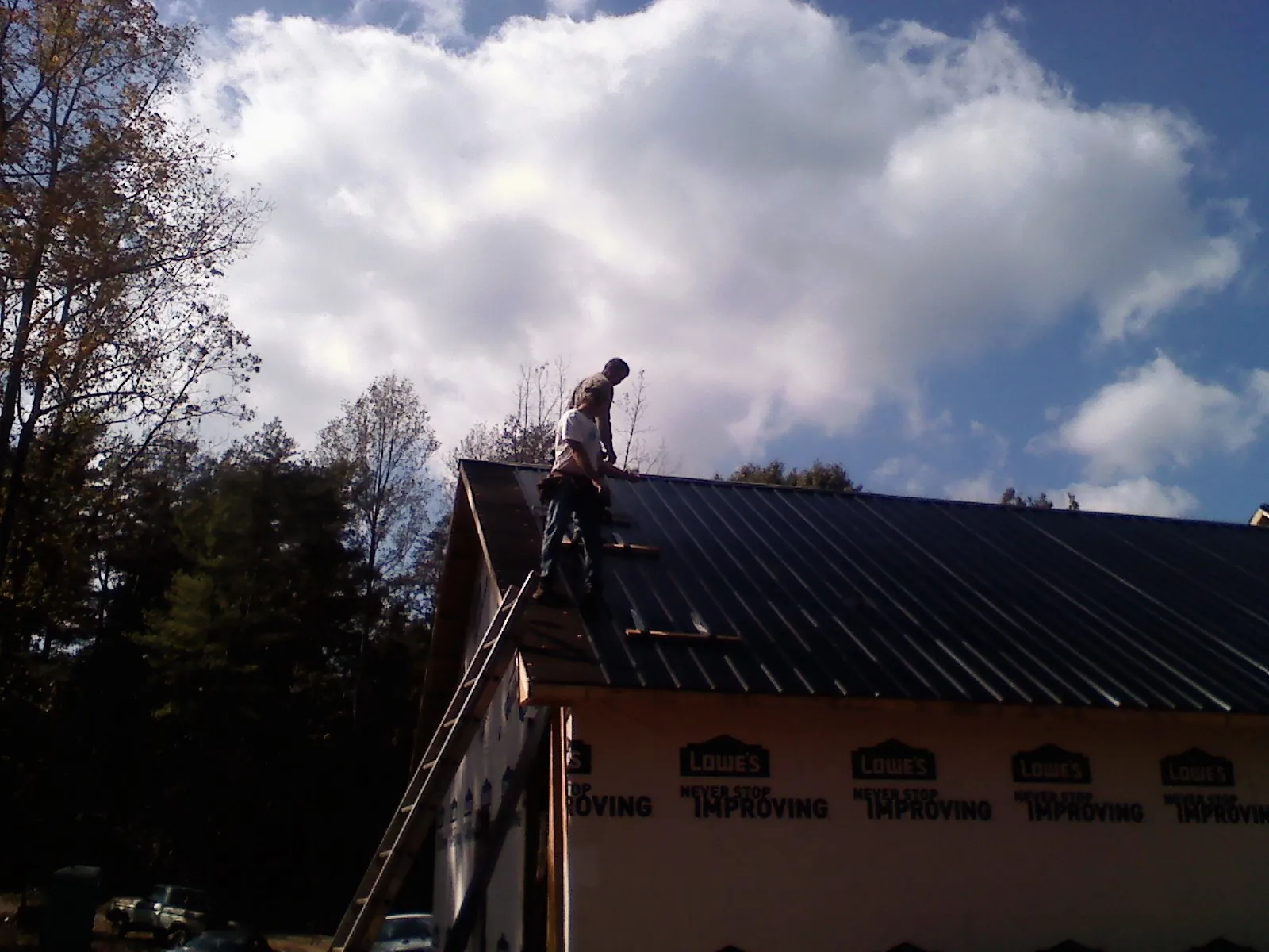 Roofer fastening dark metal panels high against a cloudy sky, from a Roof Inspection job in Tunica