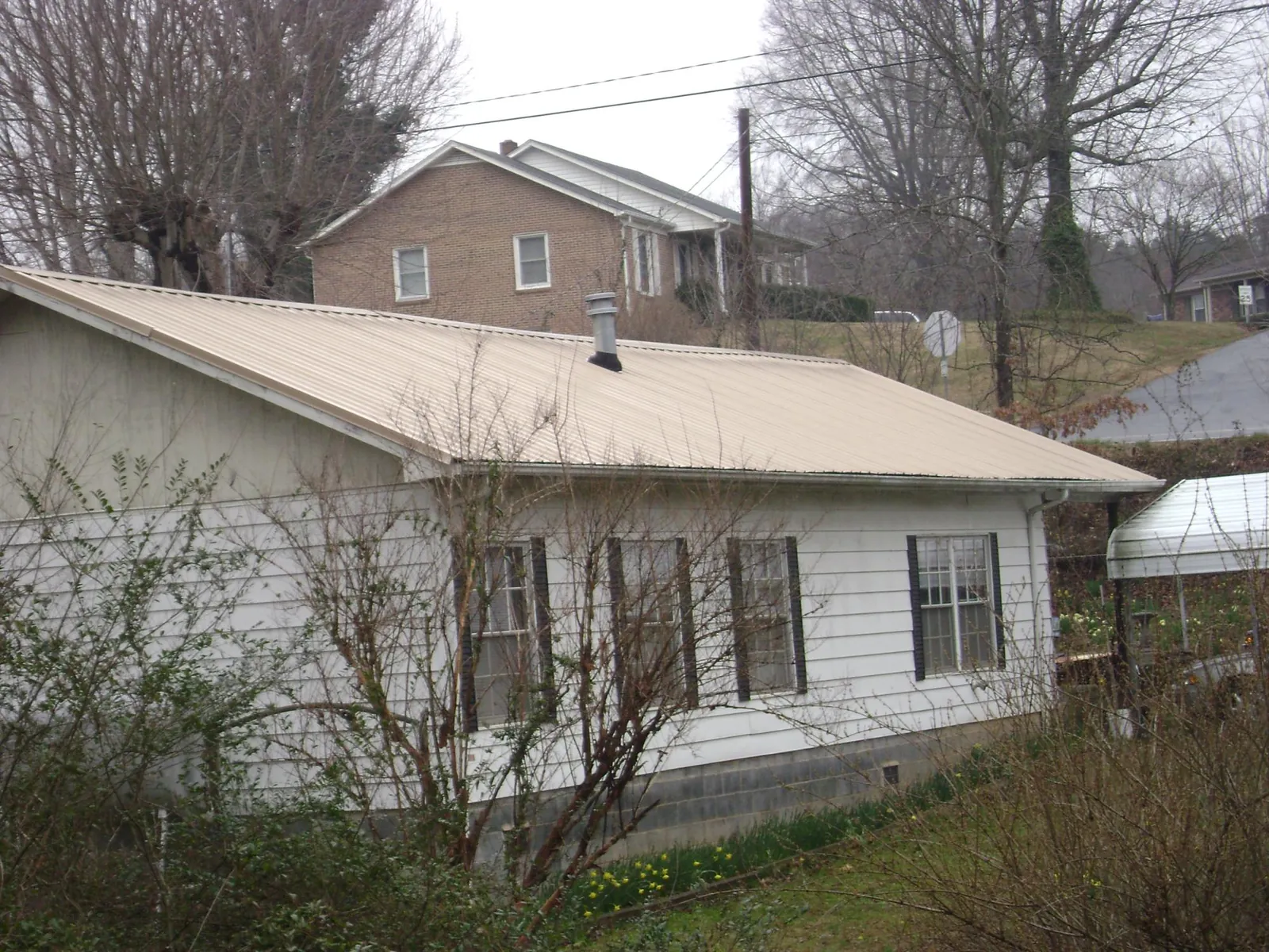 Tan metal roof on a white sided house set into a hillside — Commercial Roofing by Roofing Brothers in Tunica